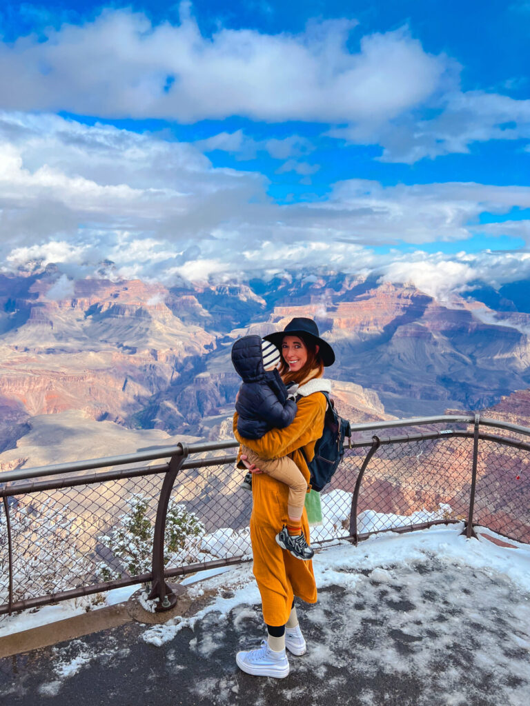 Mother holds toddler at The Grand Canyon on a winter trip 