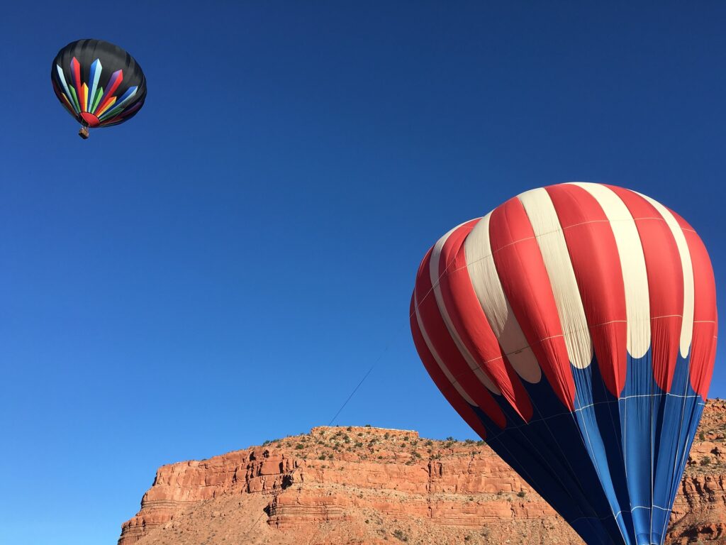 Hot air balloons flying in front of red rock cliffs